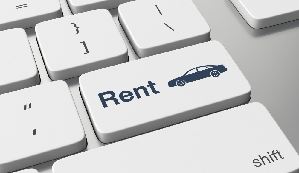 Tastatură de calculator cu o tastă inscripționată Rent și simbolul unei mașini, ilustrând rezervarea online a unui autoturism